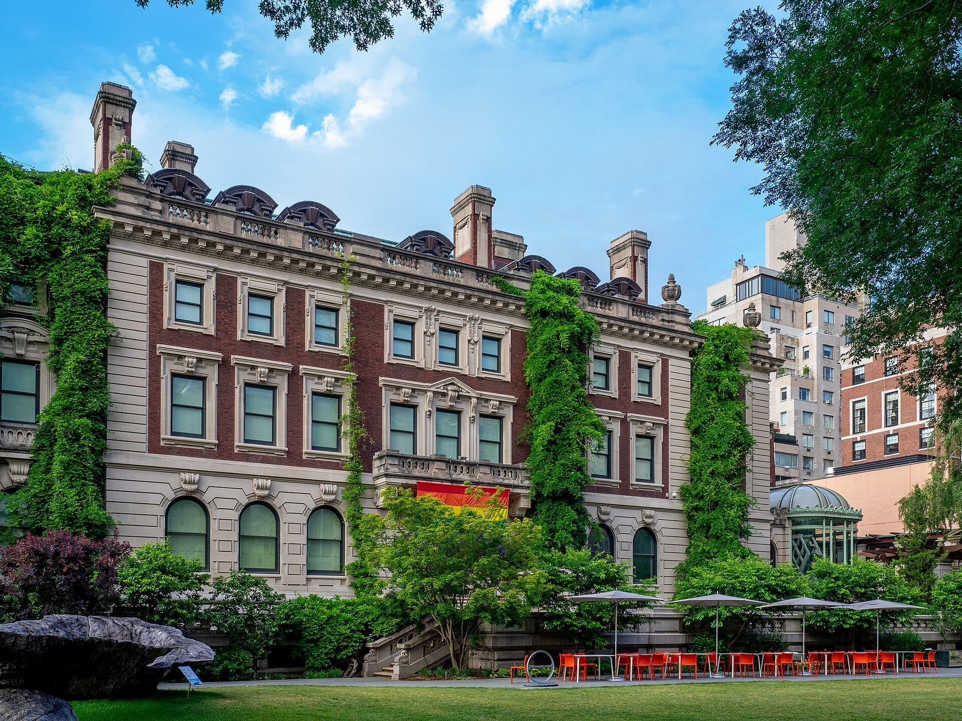 L'esterno del Cooper Hewitt, Smithsonian Design Museum presenta uno storico palazzo in mattoni coperto di edera con prato, alberi e area salotto all'aperto.