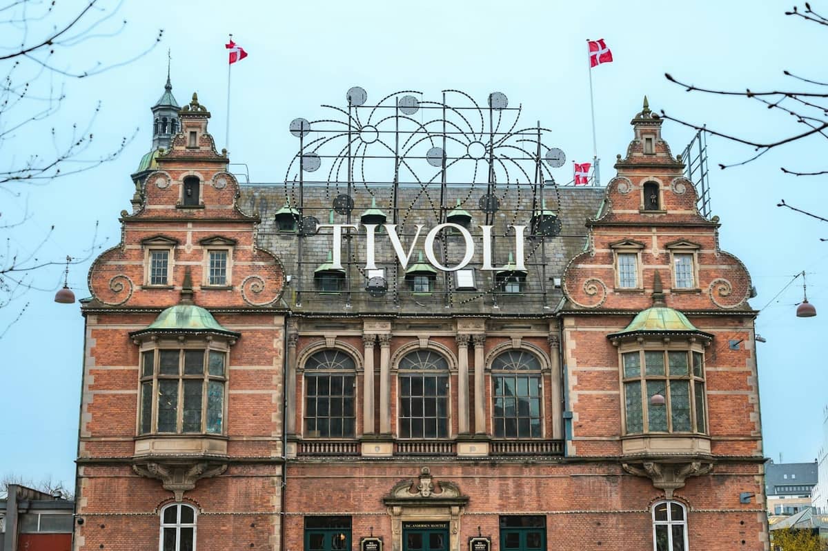 Façade principale de l'entrée de Tivoli Gardens à Copenhague avec des drapeaux danois et une enseigne emblématique, photographiée en plein jour avec une vue dégagée sur l'architecture.