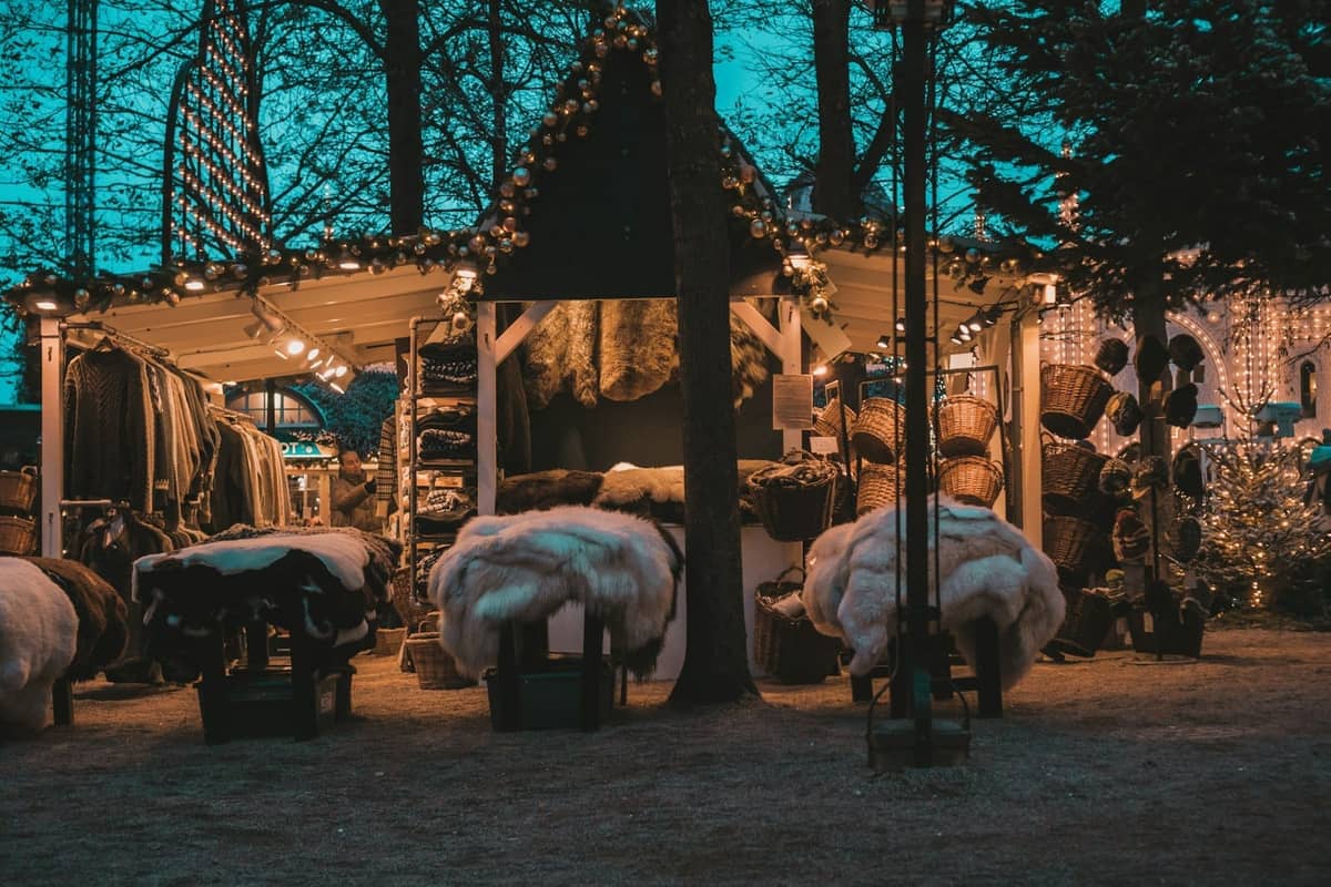 Ein gemütlicher Weihnachtsmarktstand in Kopenhagen, geschmückt mit Lichtern und mit Pelzen, Körben und festlichen Waren unter dem Abendhimmel.