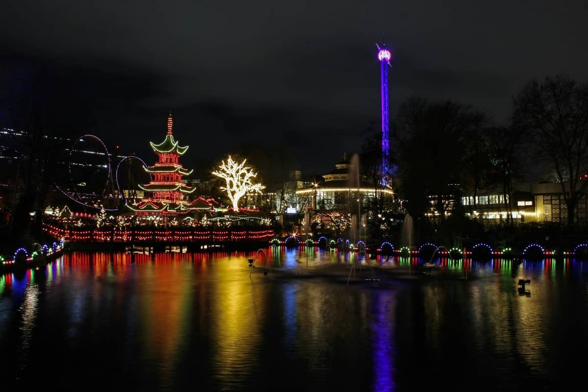Tivoli Gardens bei Nacht mit Weihnachtsbeleuchtung, bunten Spiegelungen auf dem See und beleuchtetem Pagoden in Kopenhagen.