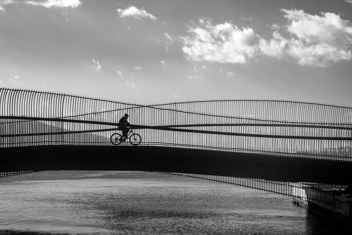 Silhouette d'un cycliste roulant sur un pont moderne et architecturalement distinctif au-dessus de l'eau à Copenhague au coucher du soleil.
