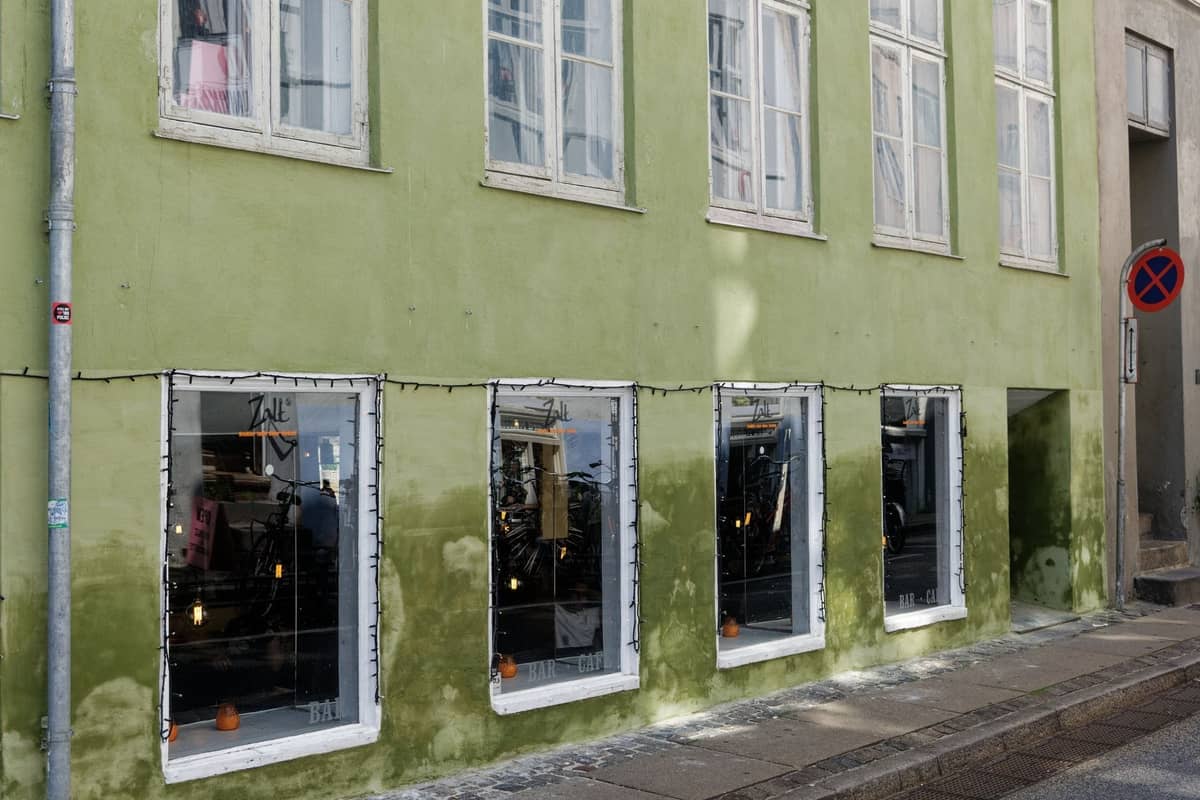 Zewnętrzna część nowoczesnej restauracji w Kopenhadze z zieloną elewacją i dużymi oknami, odbijającymi stylowe skandynawskie oświetlenie wnętrza.