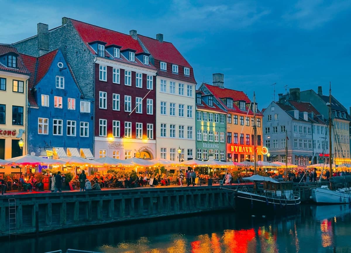 Tętniące życiem, kolorowe restauracje i kawiarnie nad kanałem w Nyhavn, Kopenhadze, z wieczornymi gośćmi i światłami odbijającymi się w wodzie.
