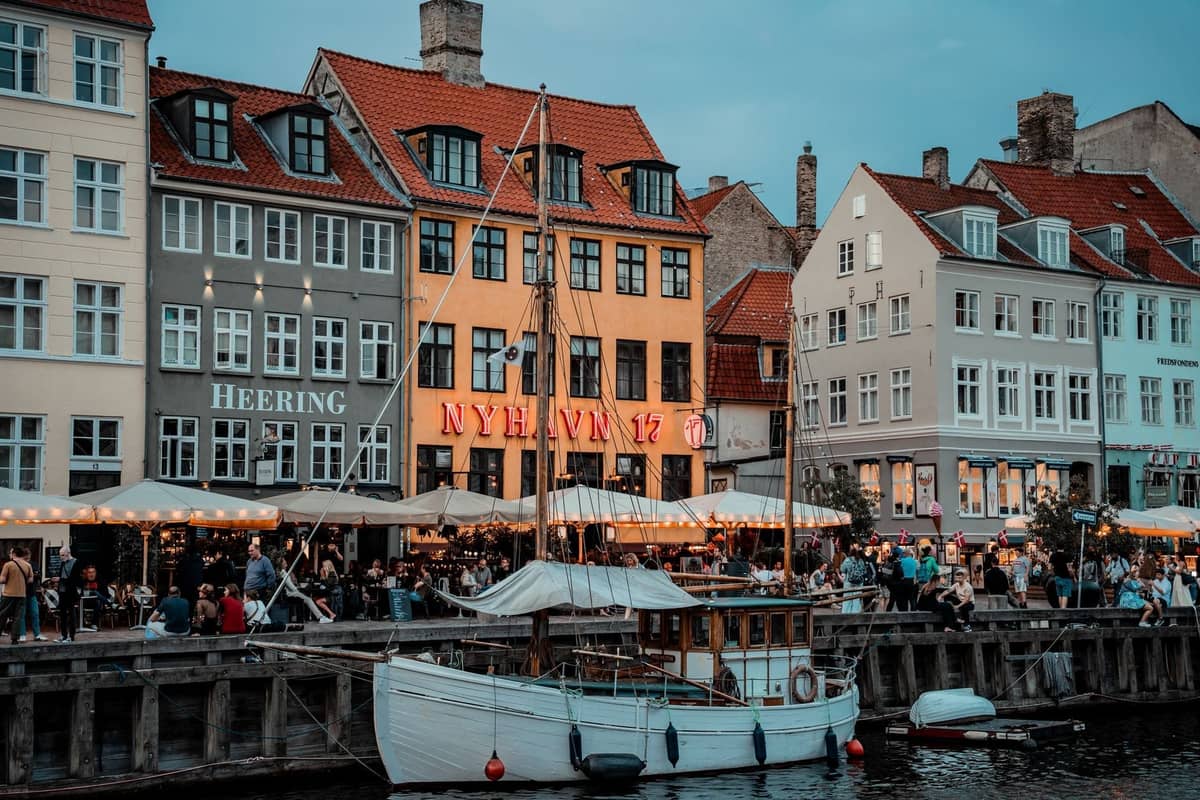 Il porto di Nyhavn a Copenaghen con ristoranti all'aperto e folle che cenano la sera accanto a colorati edifici storici.