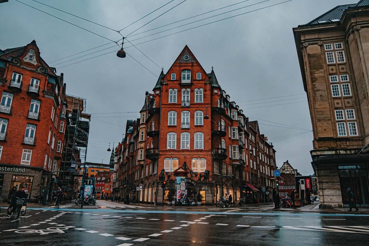 Una scena di strada piovosa nel centro di Copenaghen con classici edifici in mattoni rossi, cieli nuvolosi e pavimentazione bagnata, che cattura il tipico clima di ottobre.