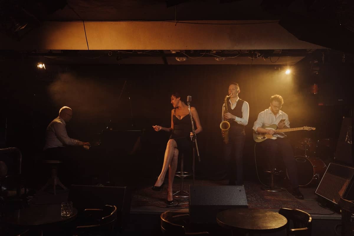 Jazzband live auf der Bühne in einem gemütlichen Club mit Klavier, Saxofon, E-Gitarre und Sängerin.