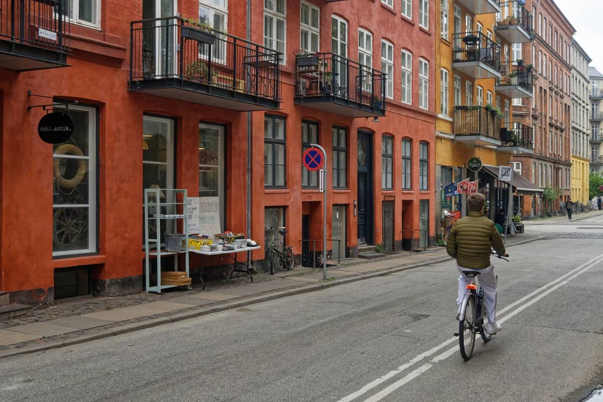 Kolorowa ulica w dzielnicy Nørrebro lub Vesterbro w Kopenhadze, z niezależnymi sklepami, balkonami apartamentów i rowerzystą przejeżdżającym obok lokalnych witryn sklepowych.