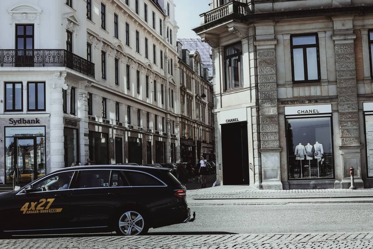 Elegancka i ekskluzywna ulica handlowa w Kopenhadze ze stylowymi witrynami sklepowymi, w tym Chanel, i taksówką przejeżdżającą po bruku. Klasyczna europejska architektura zdobi ulicę.