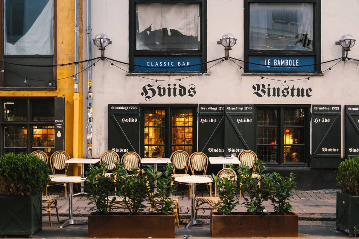 Exterior clásico del bar y restaurante Hviids Vinstue en Copenhague con terraza exterior y luces cálidas en el interior.