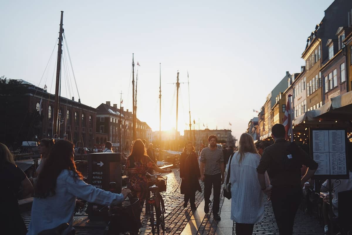 Menschen, die bei Sonnenuntergang entlang des Nyhavn-Kanals in Kopenhagen spazieren, mit historischen bunten Gebäuden und Booten entlang des Ufers.