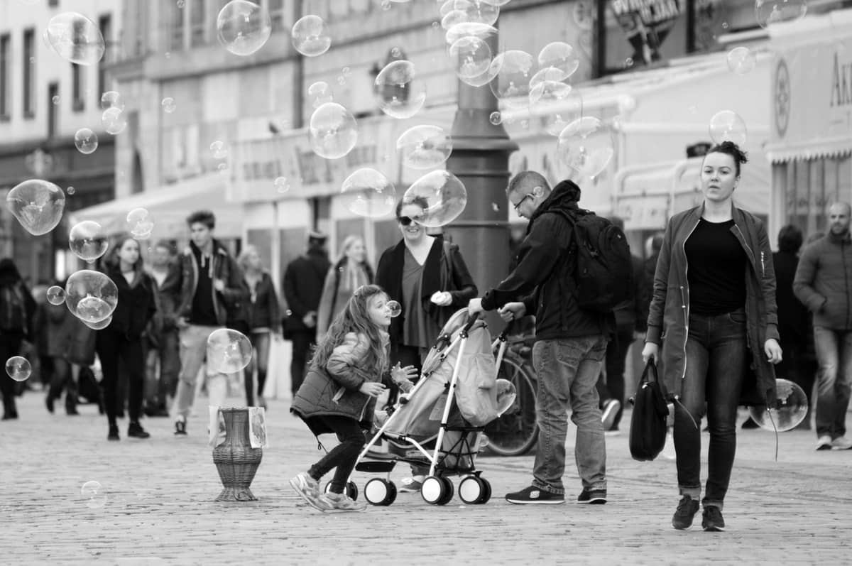 Affollata strada cittadina con famiglie, un uomo che spinge un passeggino, bambini e persone che camminano, che mostra un ambiente urbano di viaggio in famiglia.