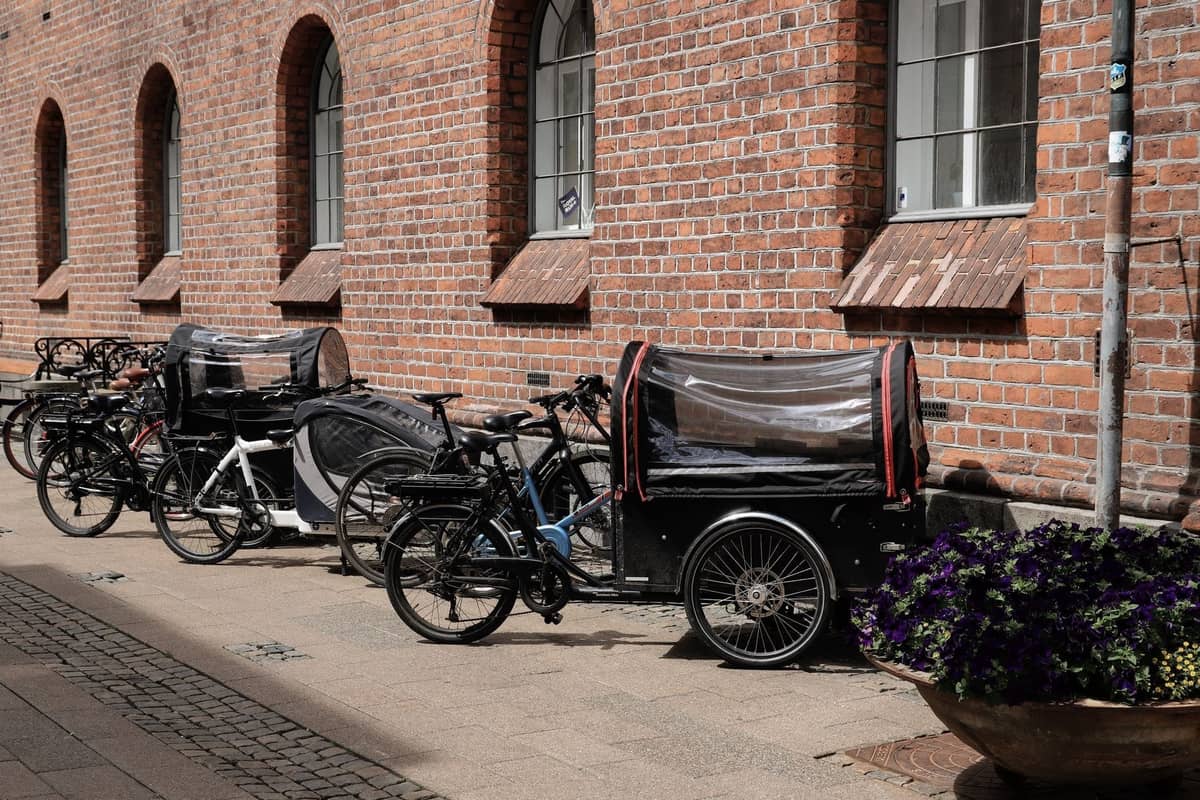 Cargo bike progettate per trasportare bambini e famiglie sono parcheggiate lungo una tranquilla strada acciottolata con un edificio in mattoni a Copenaghen.
