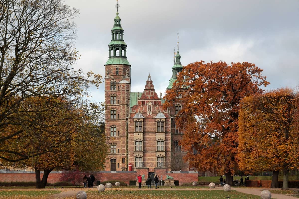 Vista del Castello di Rosenborg a Copenaghen con famiglie e bambini che passeggiano e giocano nel parco tra gli alberi autunnali.