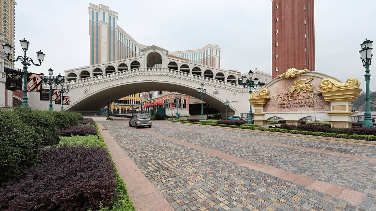 Außenansicht des Resorts The Venetian Macao mit seinem ikonischen Schriftzug und einer Nachbildung der Rialtobrücke in Venedig, umgeben von prächtigen Gebäuden und eleganten Laternen.