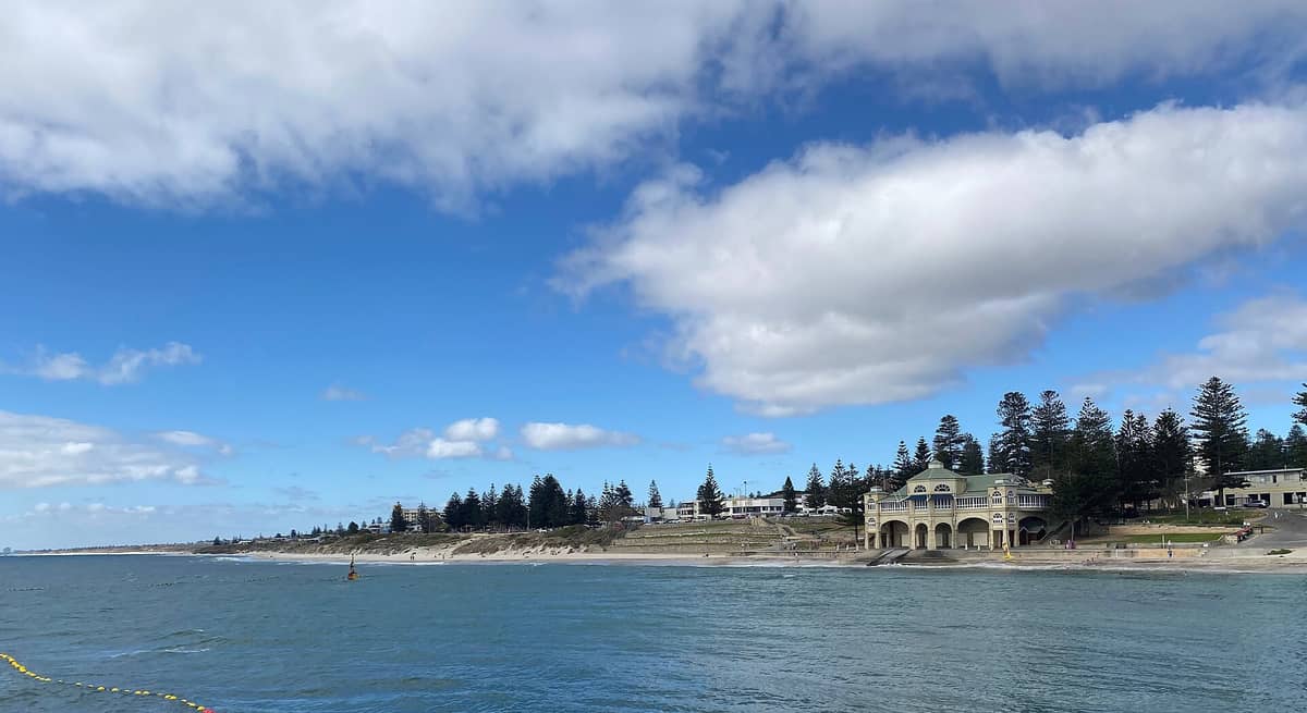 ชายหาด Cottesloe ในเพิร์ธ มองเห็น Indiana Teahouse อันโด่งดังริมทะเล ต้นสน ริมหาดทราย และท้องทะเลฟ้าครามใต้ท้องฟ้าโปร่งบางส่วน
