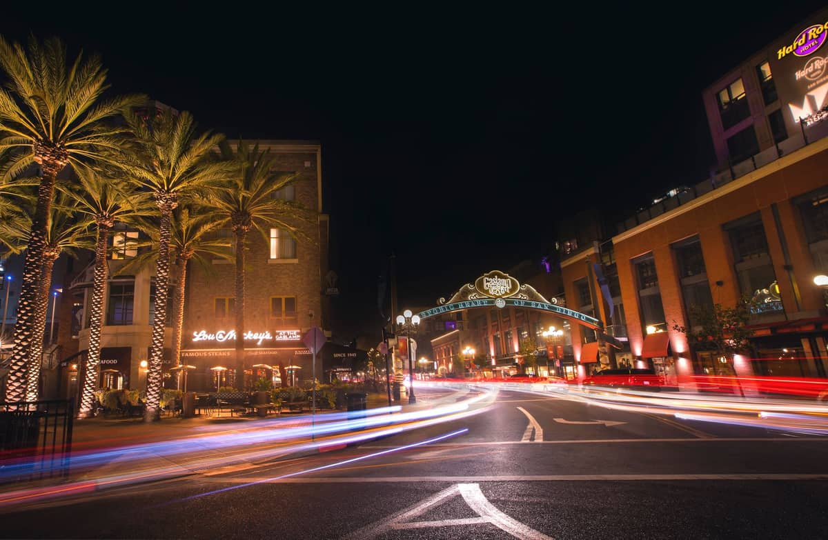 Nächtliche Ansicht des historischen Gaslamp Quarter in San Diego mit Palmen, Neonlichtern und dem ikonischen Gaslamp-Schild über einer belebten Straße.