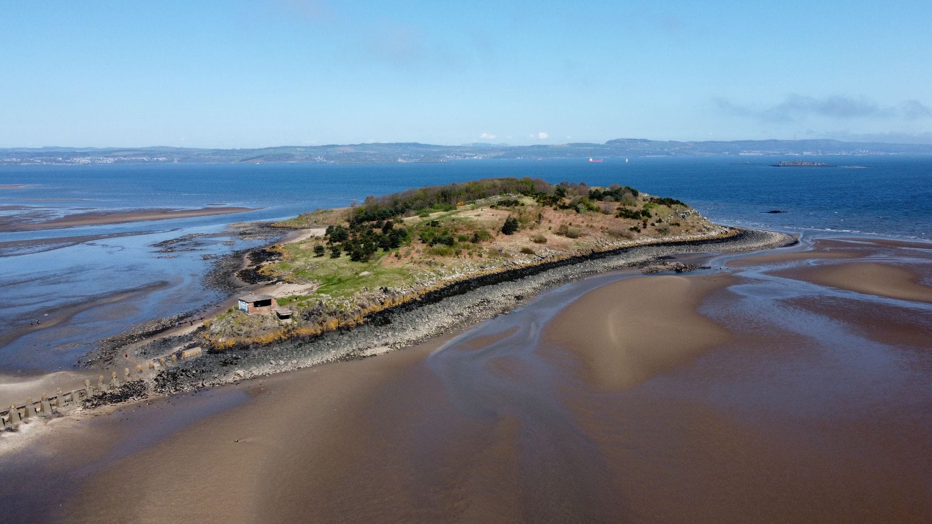 Luftaufnahme von Cramond Island bei Ebbe mit dem sandigen Gezeitendamm, Kriegsbauwerken und grüner Vegetation vor dem Hintergrund des Firth of Forth.