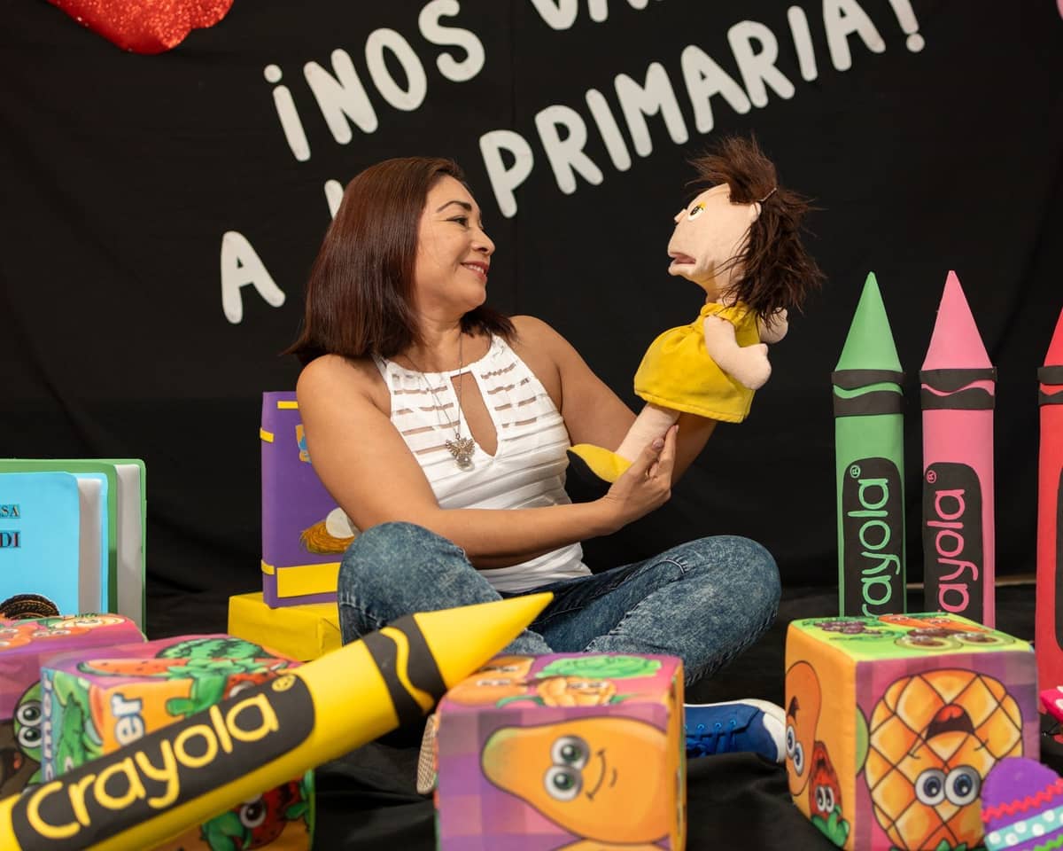 Frau, die mit einer Puppe sitzt, umgeben von großen bunten Crayola-Buntstift-Requisiten und verspielten Blöcken im Crayola Experience Orlando.