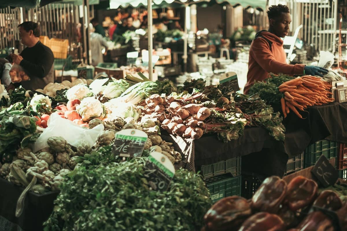 Animado mercado al aire libre en Creta con vendedores que ofrecen verduras frescas de temporada como alcachofas, zanahorias, verduras y hierbas en exhibición.