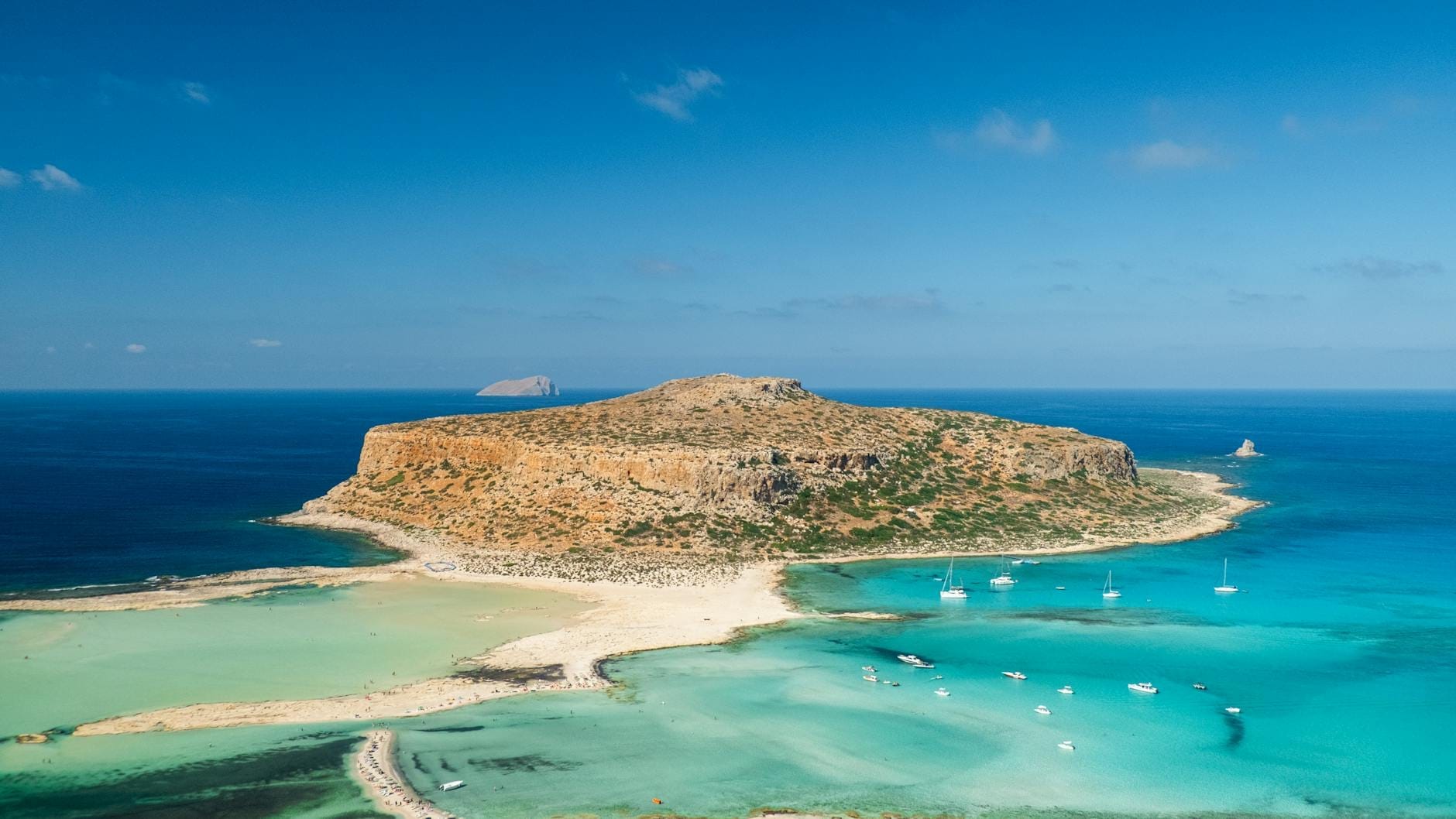 Vista deslumbrante da laguna turquesa de Balos com seu istmo de areia branca e vários barcos ancorados nas águas cristalinas, Creta, Grécia.