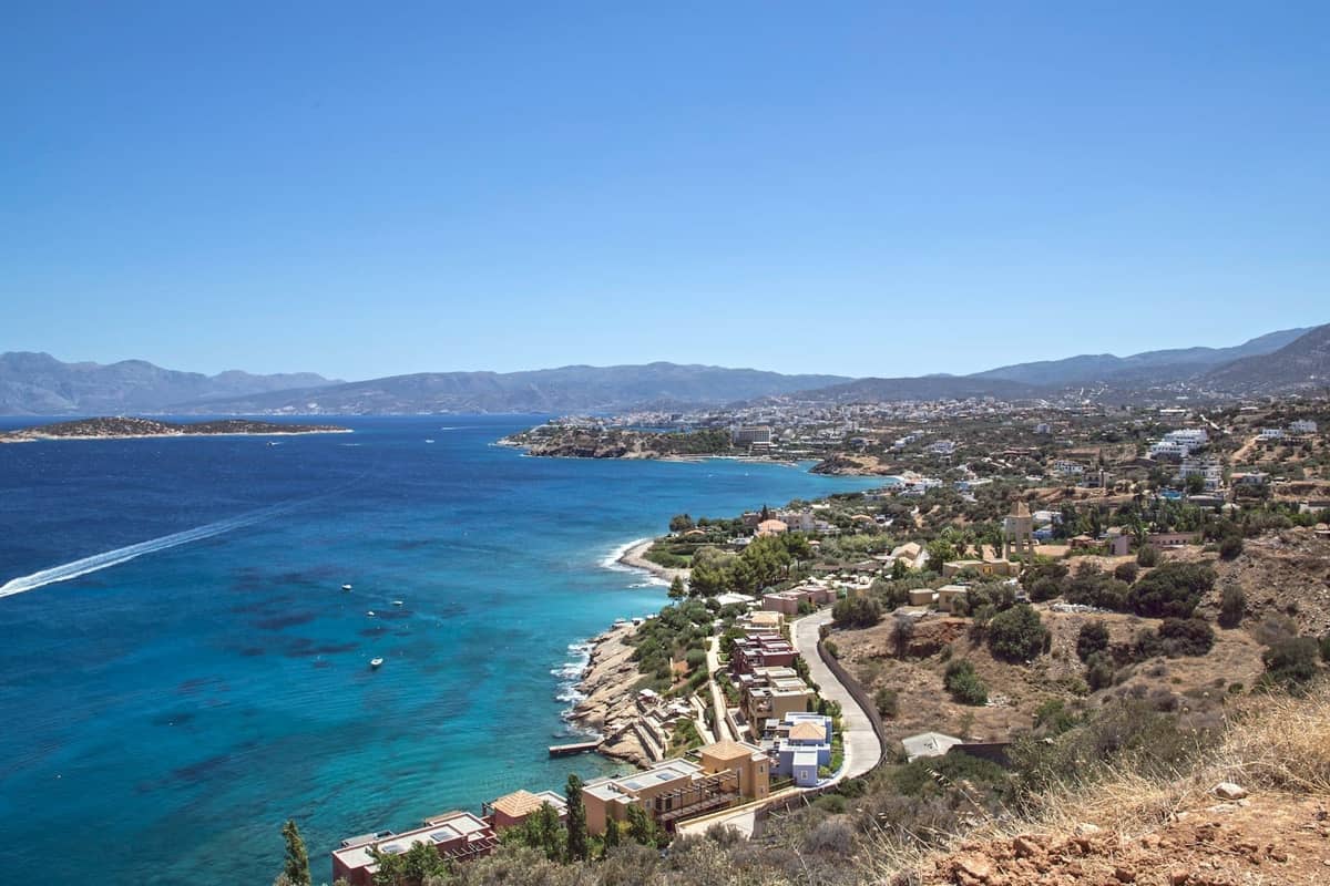 Amplia vista costera de Creta con mar azul cristalino, cielos soleados y pueblos costeros a lo largo de la orilla bajo el clima de octubre.