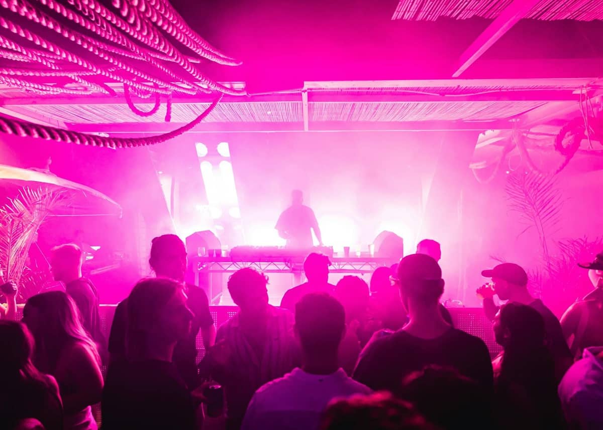 Tłum tańczący i bawiący się podczas występu DJ-a w tętniącej życiem atmosferze klubu z neonowym oświetleniem