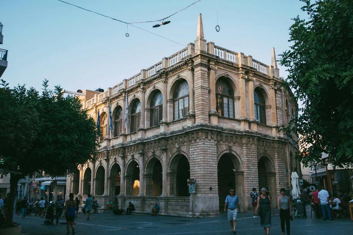 Historyczny budynek Loggia w Heraklionie i plac dla pieszych o zmierzchu, z ludźmi spacerującymi i gromadzącymi się w centrum miasta.