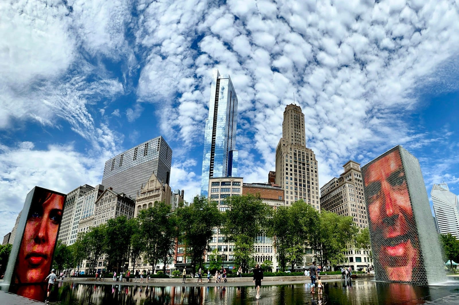 Crown Fountain nel Millennium Park di Chicago con volti digitali su torri di vetro, vasca riflettente, grattacieli della città e persone che godono di una giornata di sole.