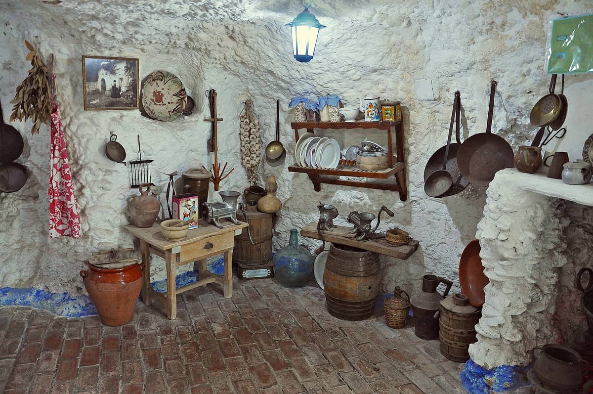 ภายในบ้านถ้ำที่ Cuevas del Sacromonte ในเมือง Granada แสดงให้เห็นเครื่องมือครัวแบบชนบท เครื่องปั้นดินเผา ชั้นวางของ และผนังหินใต้แสงโคมไฟ