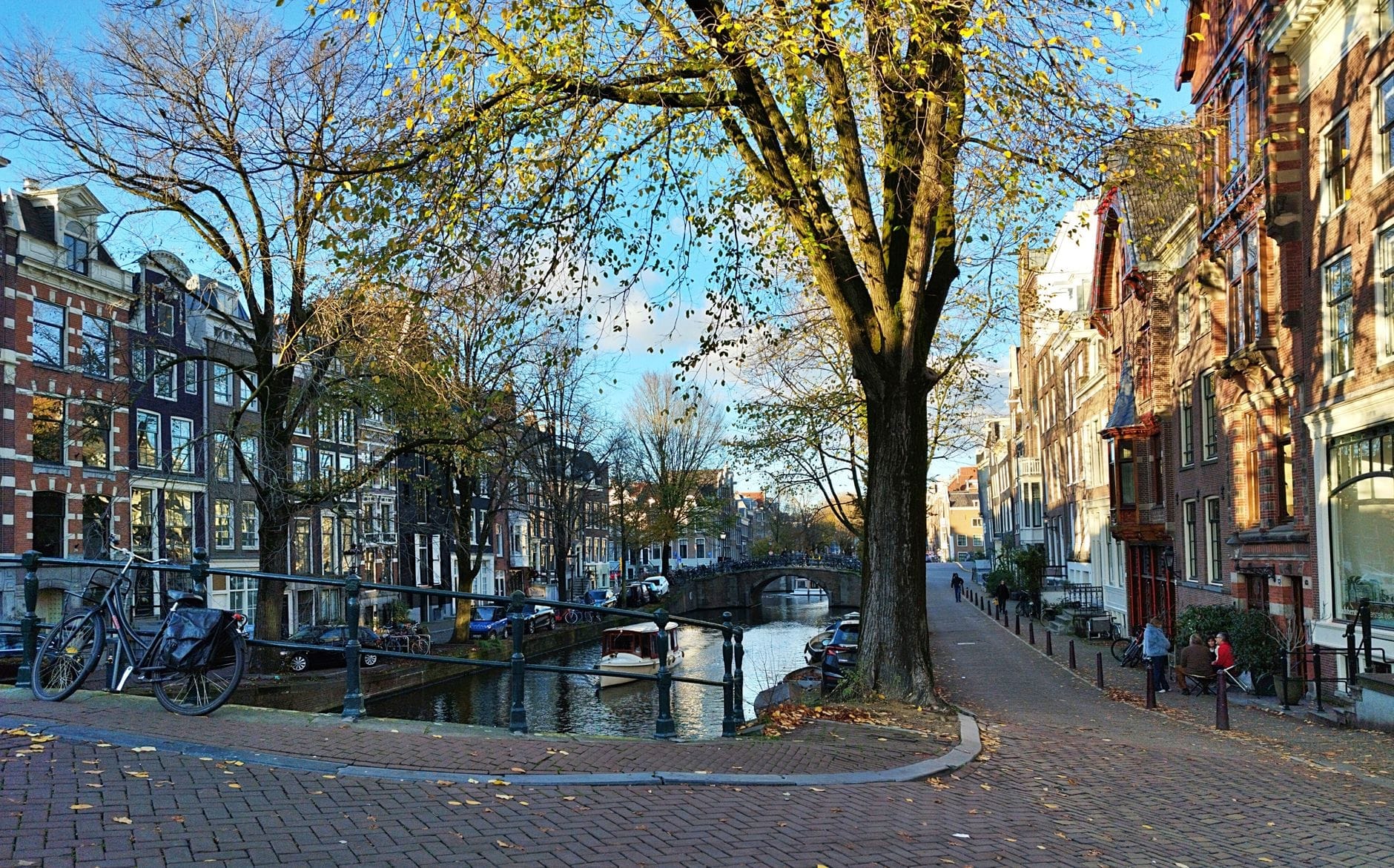Una calle junto al canal en Ámsterdam con bicicletas aparcadas, casas holandesas clásicas, un puente y caminos bordeados de árboles, ideal para rutas ciclistas urbanas.