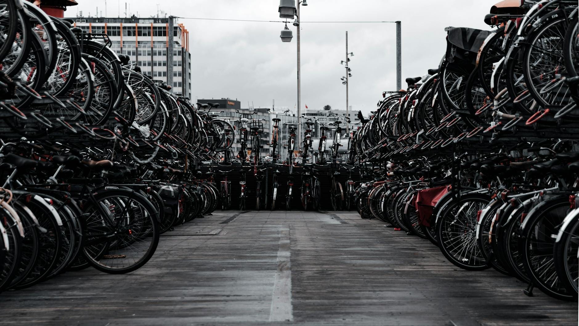 Filas de bicicletas aparcadas en un estacionamiento de bicicletas de varios niveles en Ámsterdam con edificios urbanos al fondo.
