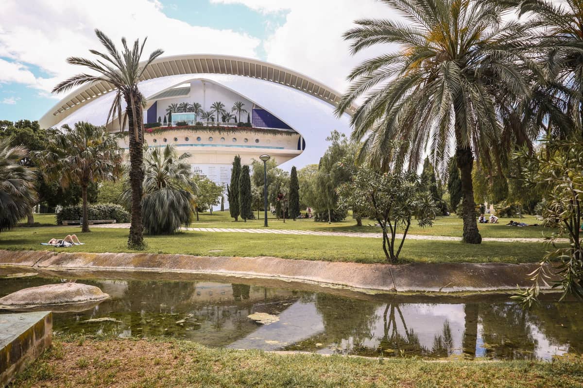 Lussureggiante parco con palme e il moderno Palau de les Arts Reina Sofia bianco visibile sullo sfondo, parte del Giardino del Turia a Valencia.