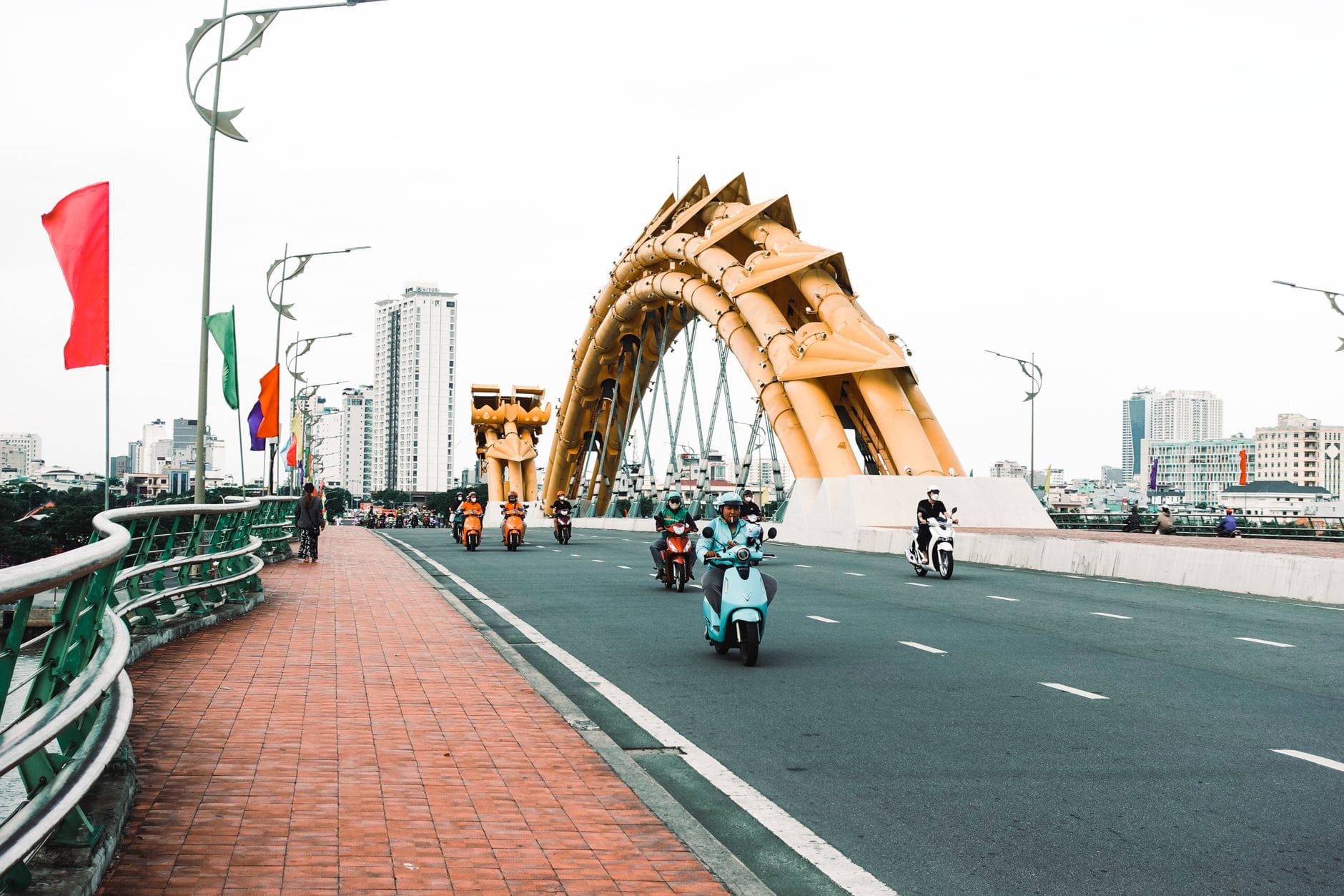 วิวกว้างของ Dragon Bridge ในดานังพร้อมสกูตเตอร์และมอเตอร์ไซค์ที่มุ่งหน้าสู่ใจกลางเมือง มีอาคารสูงเป็นฉากหลัง