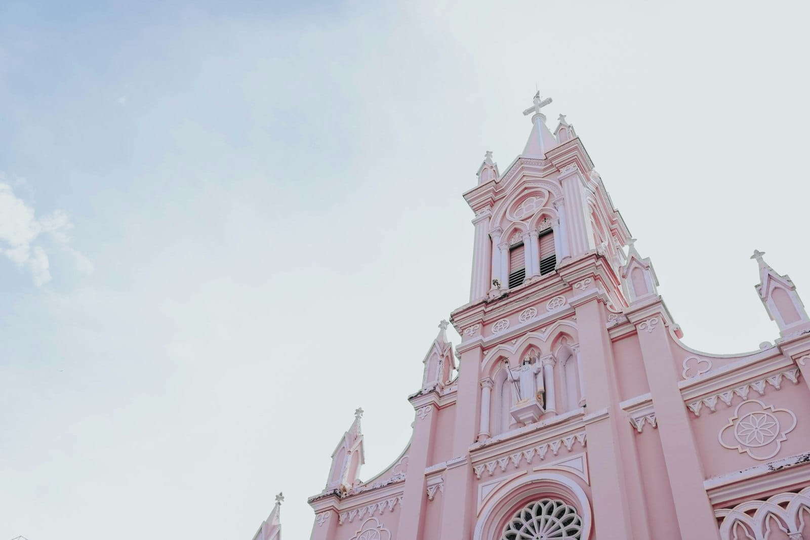 ด้านหน้าอาคารสีชมพูพาสเทลและยอดแหลมโกธิกประดับประดาของ Da Nang Cathedral โดดเด่นสะดุดตาบนท้องฟ้าใส