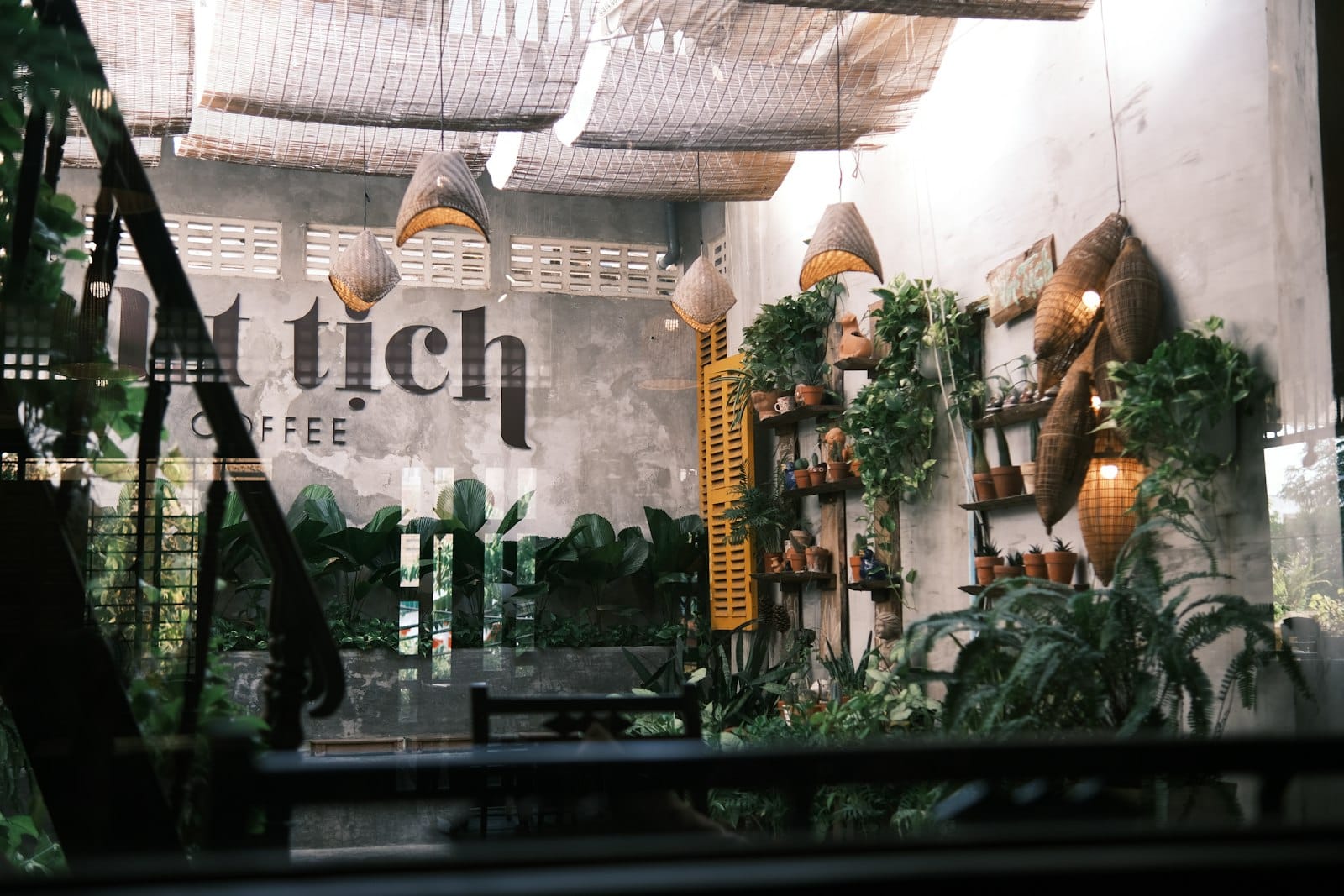 บรรยากาศในร้านกาแฟดานังสุดร่มรื่น ตกแต่งด้วยโคมหวายและต้นไม้ มีป้าย 'tich coffee' บนผนังในร้านที่โปร่งสว่าง