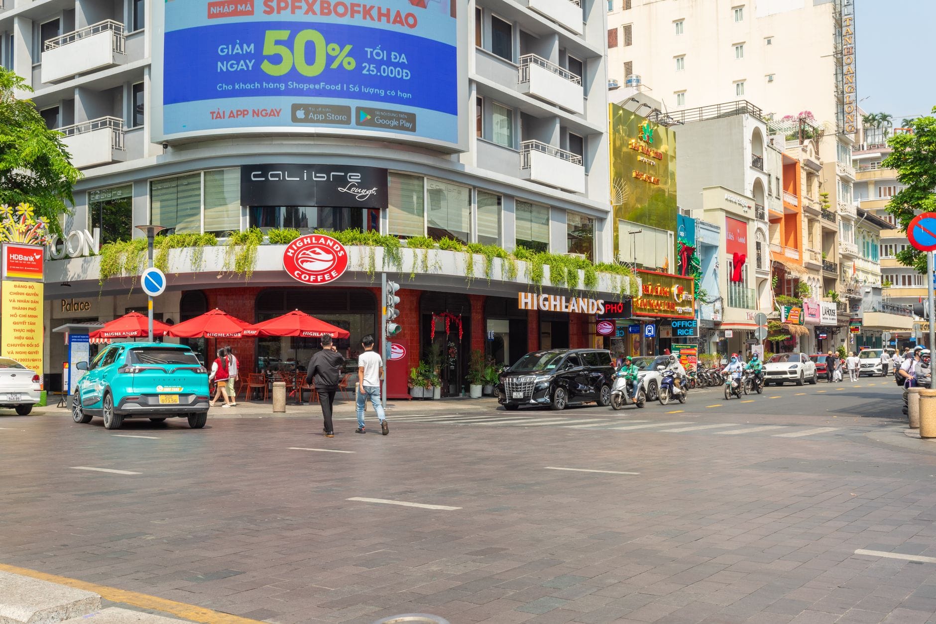ฉากถนนใน Da Nang มีผู้คนเดินใกล้ร้านกาแฟและแท็กซี่จอดอยู่ด้านหน้า พร้อมอาคารเมืองสมัยใหม่ที่มองเห็นได้ชัดเจน