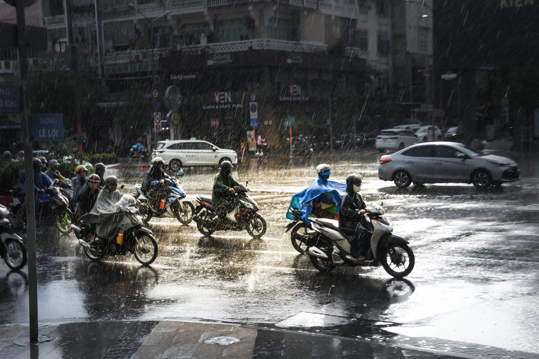 รถมอเตอร์ไซค์แล่นฝ่าสายฝนตกหนักบนถนนที่คึกคักในเมืองดานัง โดยมองเห็นพื้นถนนเปียกและสายฝนได้อย่างชัดเจน