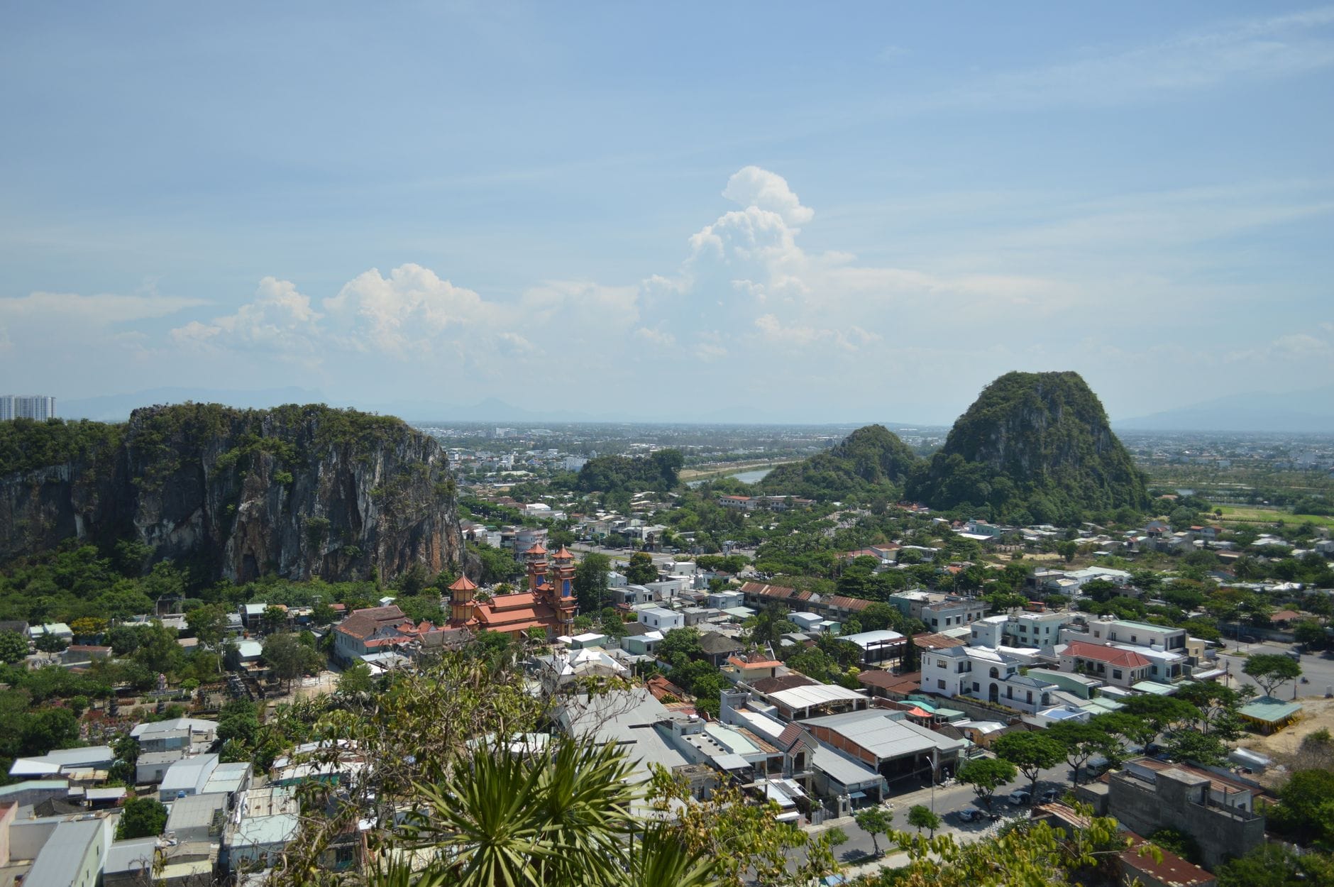 วิวทิวทัศน์ของ Marble Mountains ที่มียอดหินปูนสูงตระหง่านเหนือหลังคาบ้านเมือง Da Nang และต้นไม้สีเขียวภายใต้ท้องฟ้าสีฟ้า