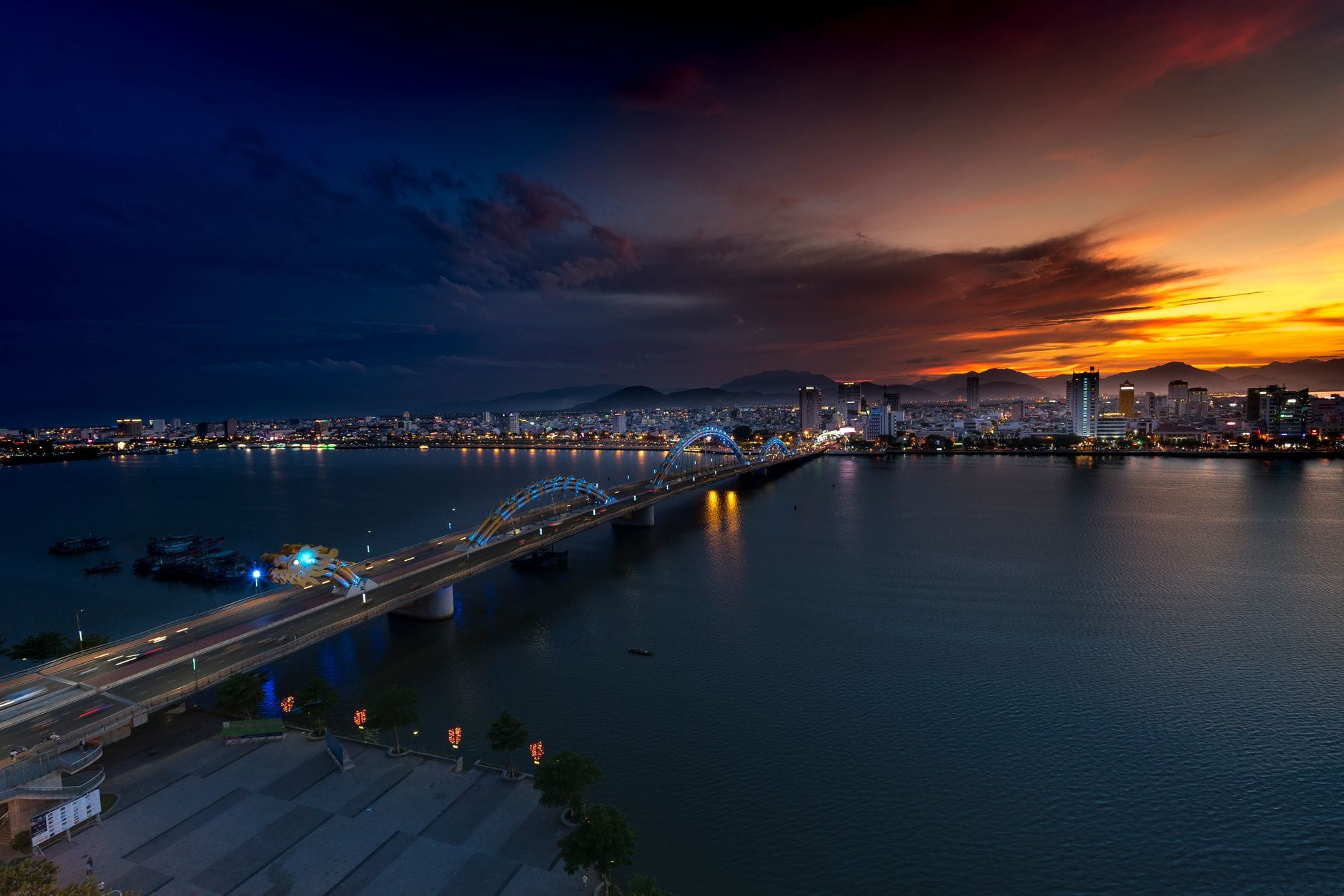 วิวภูมิทัศน์ของ Dragon Bridge และเส้นขอบฟ้าเมือง Da Nang ยามพระอาทิตย์ตกพร้อมแสงไฟของเมืองสะท้อนบนแม่น้ำ
