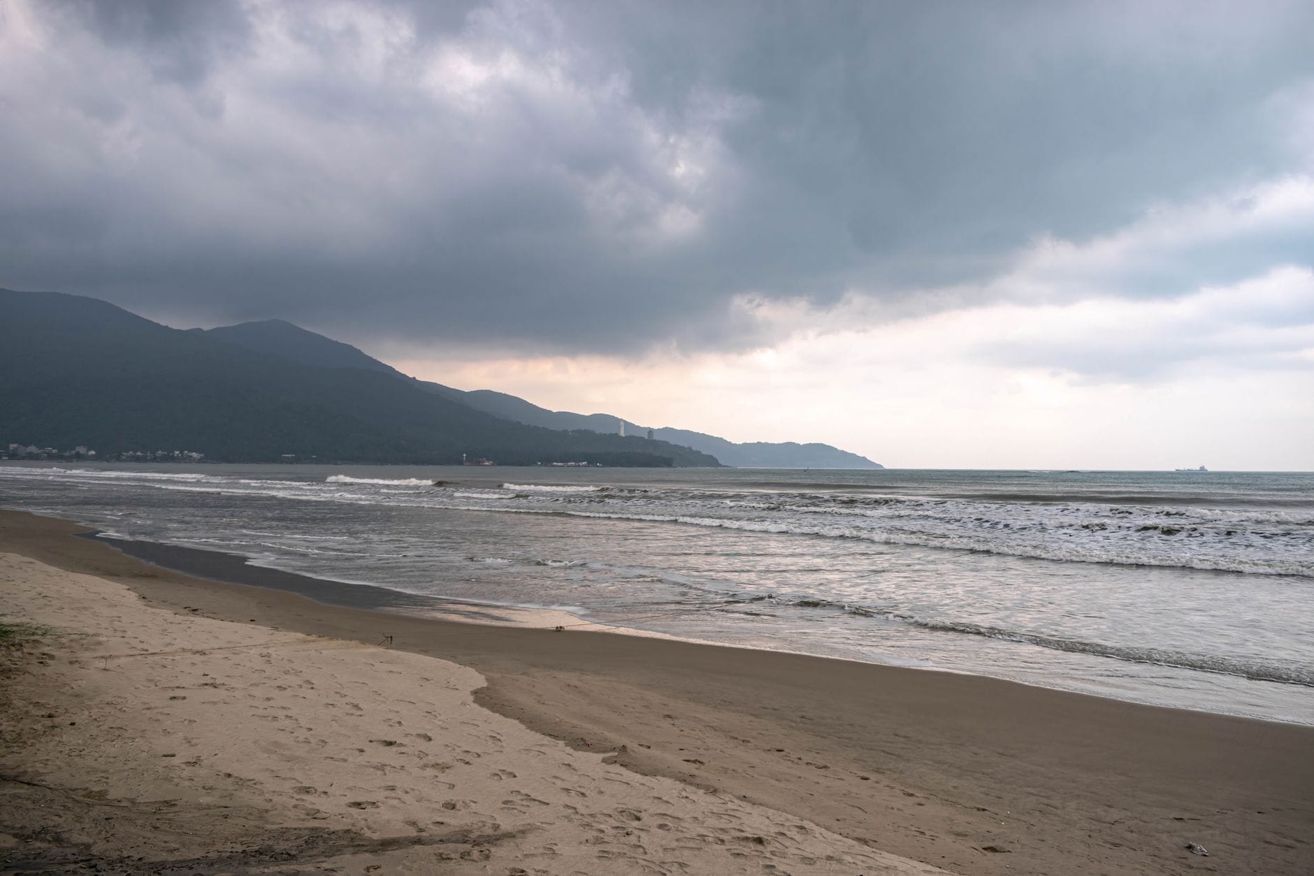 ท้องฟ้าครึ้มและเมฆพายุสีเข้มเหนือชายหาดทรายและทะเลคลื่นแรงใกล้ดานัง แสดงให้เห็นถึงความเสี่ยงด้านสภาพอากาศตามฤดูกาล