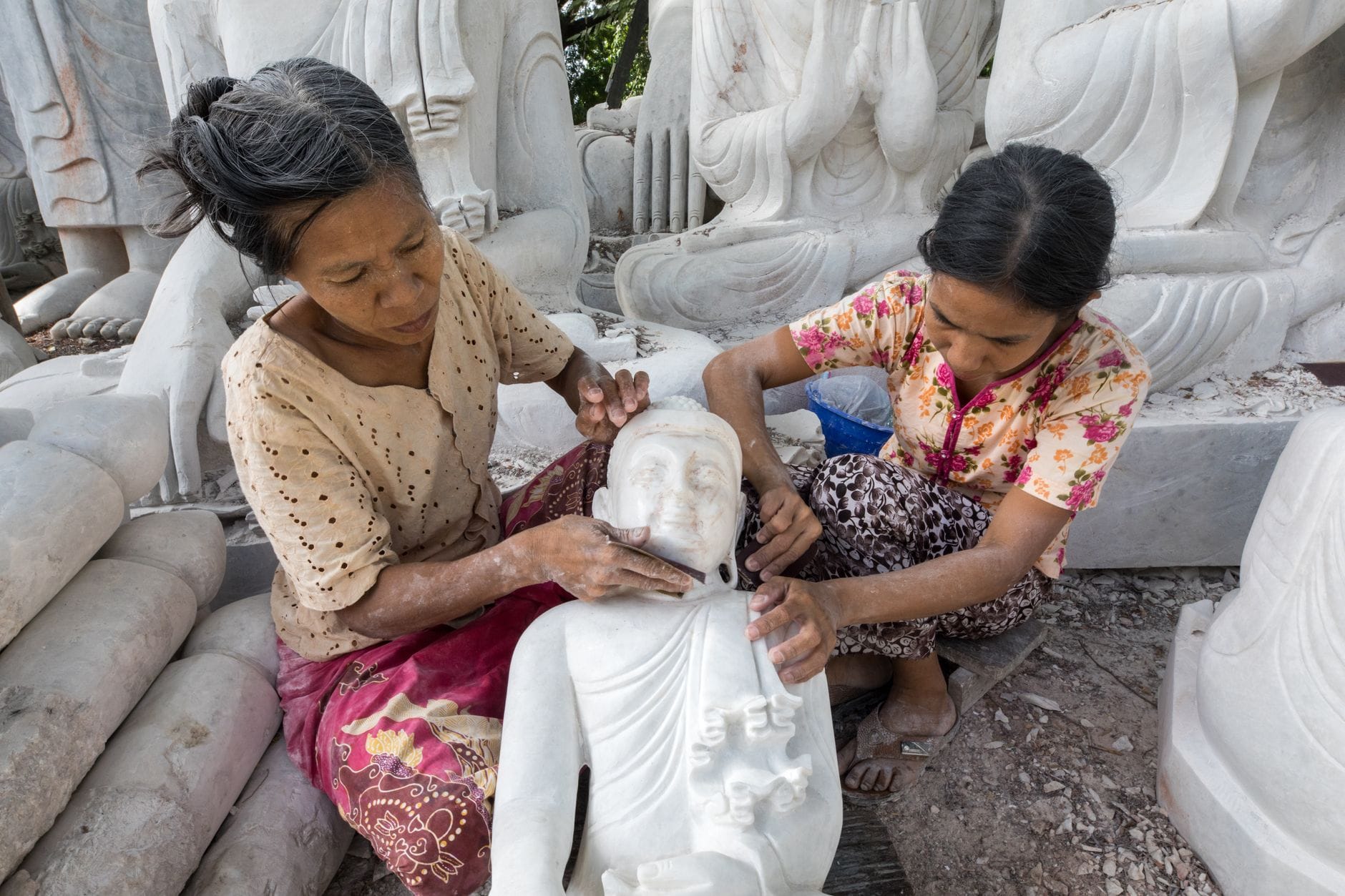 ผู้หญิงสองคนกำลังแกะสลักพระพุทธรูปหินอ่อนที่ล้อมรอบด้วยประติมากรรมหินอ่อนชิ้นอื่นๆ แสดงให้เห็นถึงเวิร์กช็อปแกะสลักหินอ่อนชื่อดังของ Da Nang