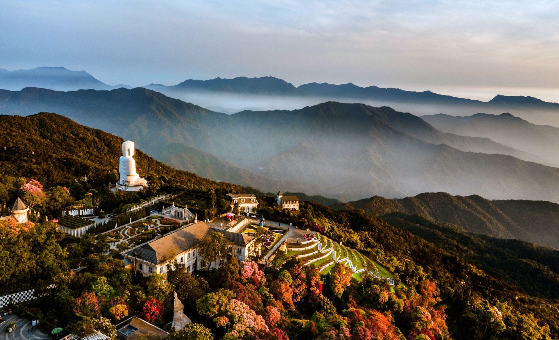 มุมมองทางอากาศของ Ba Na Hills พร้อมภูเขา พระพุทธรูป ต้นไม้หลากสีสัน และหมอกยามเช้าใกล้กับ Da Nang
