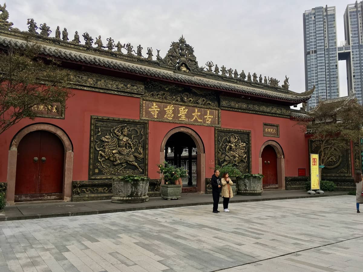 Frontansicht des Daci-Tempels in Chengdu mit prunkvollen roten Wänden, goldenen Schnitzereien und Besuchern, die an einem bewölkten Tag am Eingang stehen.