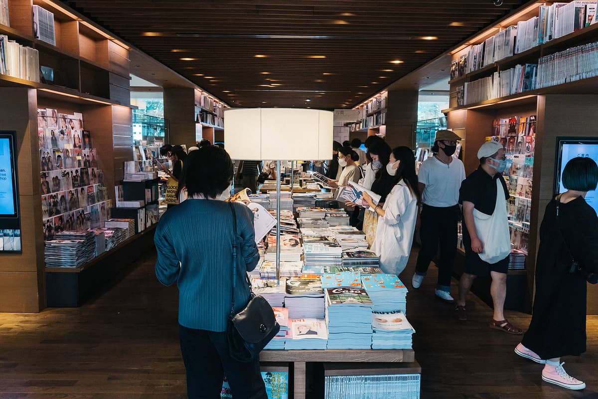 Interior of Daikanyama Tsutaya Books at Daikanyama T-Site, with people browsing magazines and books on large wooden tables and shelves.