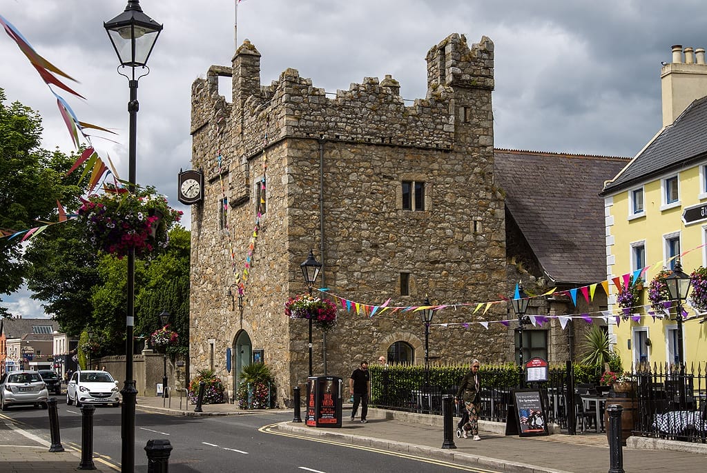 Dalkey Castle & Heritage Centre a Dublino, una torre medievale in pietra con merli, vivaci bandierine e colorati edifici vicini in una strada animata.