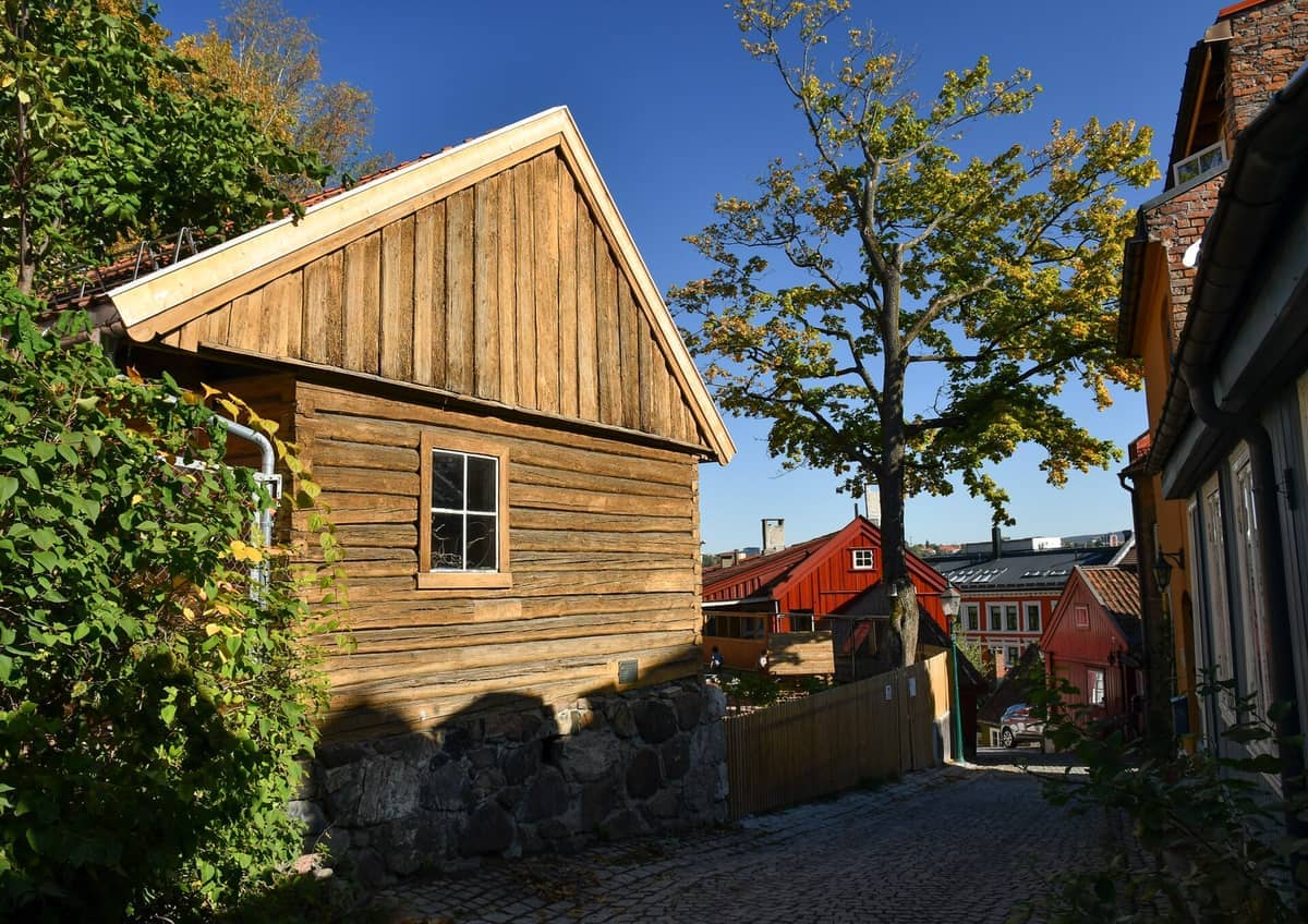 บ้านไม้แบบดั้งเดิมและถนนหินกรวดในวันที่แดดสดใสที่ Damstredet, Oslo ล้อมรอบด้วยต้นไม้เขียวขจีและท้องฟ้าสีฟ้า
