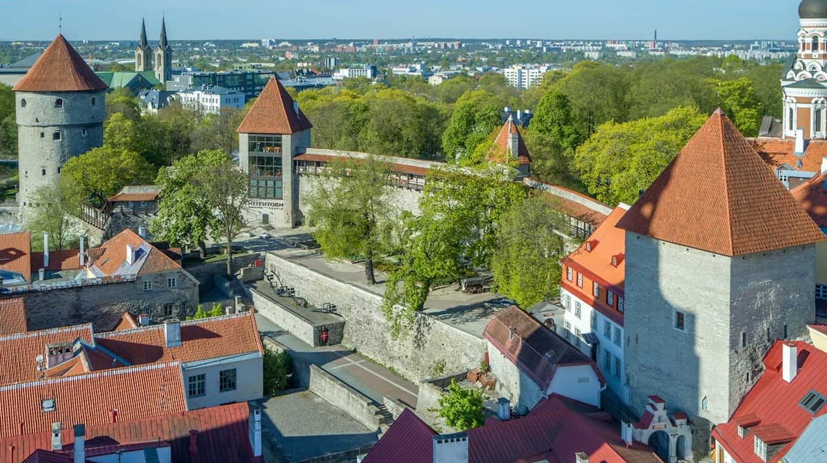 Luftaufnahme des Dänischen Königsgartens in Tallinn mit mittelalterlichen Steinmauern, Türmen mit roten Dächern, üppigen Bäumen und umgebenden Altstadtgebäuden.