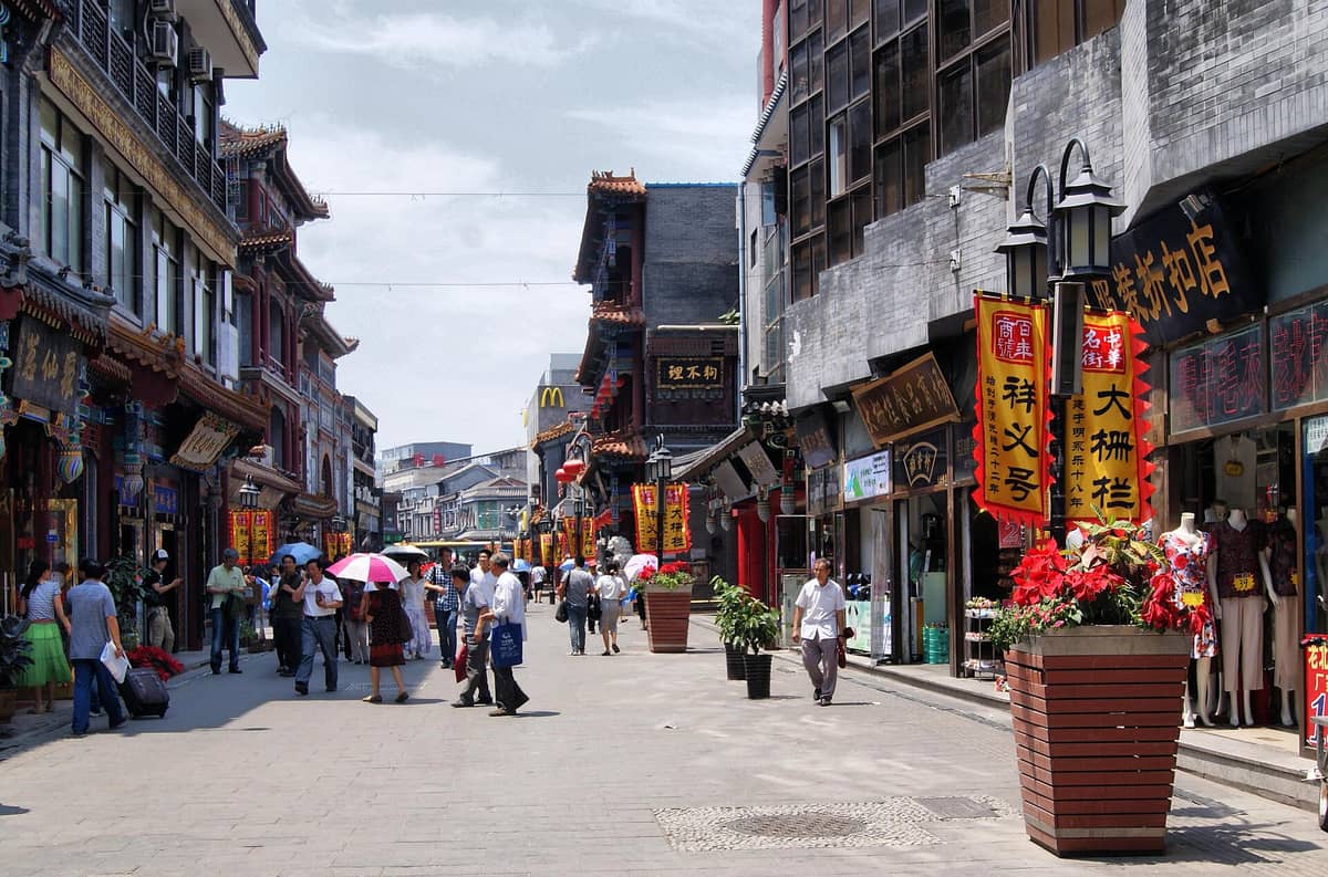 Blick auf die Dashilar-Straße in Peking bei Tag: Menschen schlendern durch eine traditionelle Handelsstraße, gesäumt von historischen Läden und dekorierten Ladenschildern.