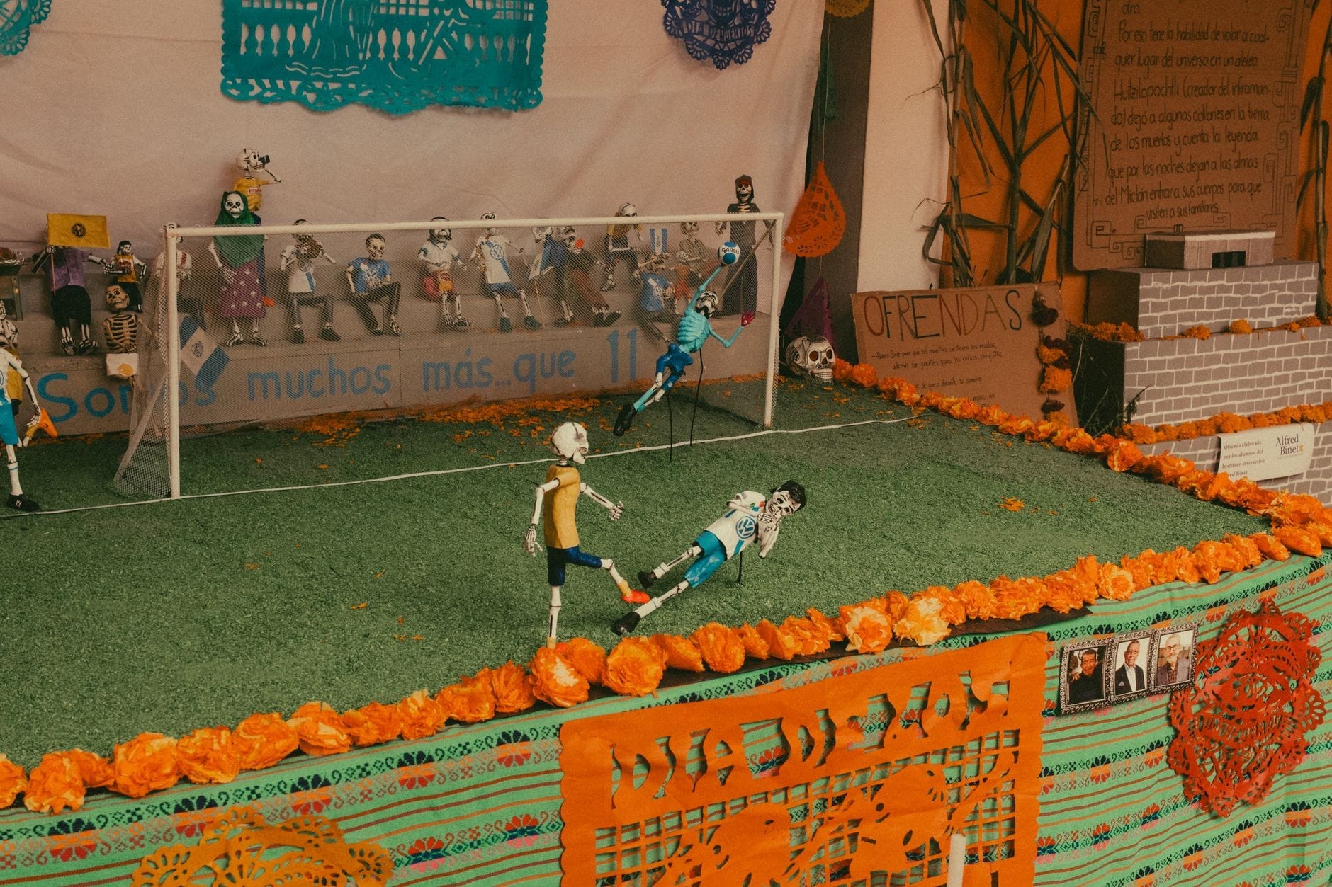 Um colorido altar comunitário do Día de los Muertos montado ao ar livre, decorado com malmequeres e recortes de papel, com esqueletos jogadores de futebol divertidos.