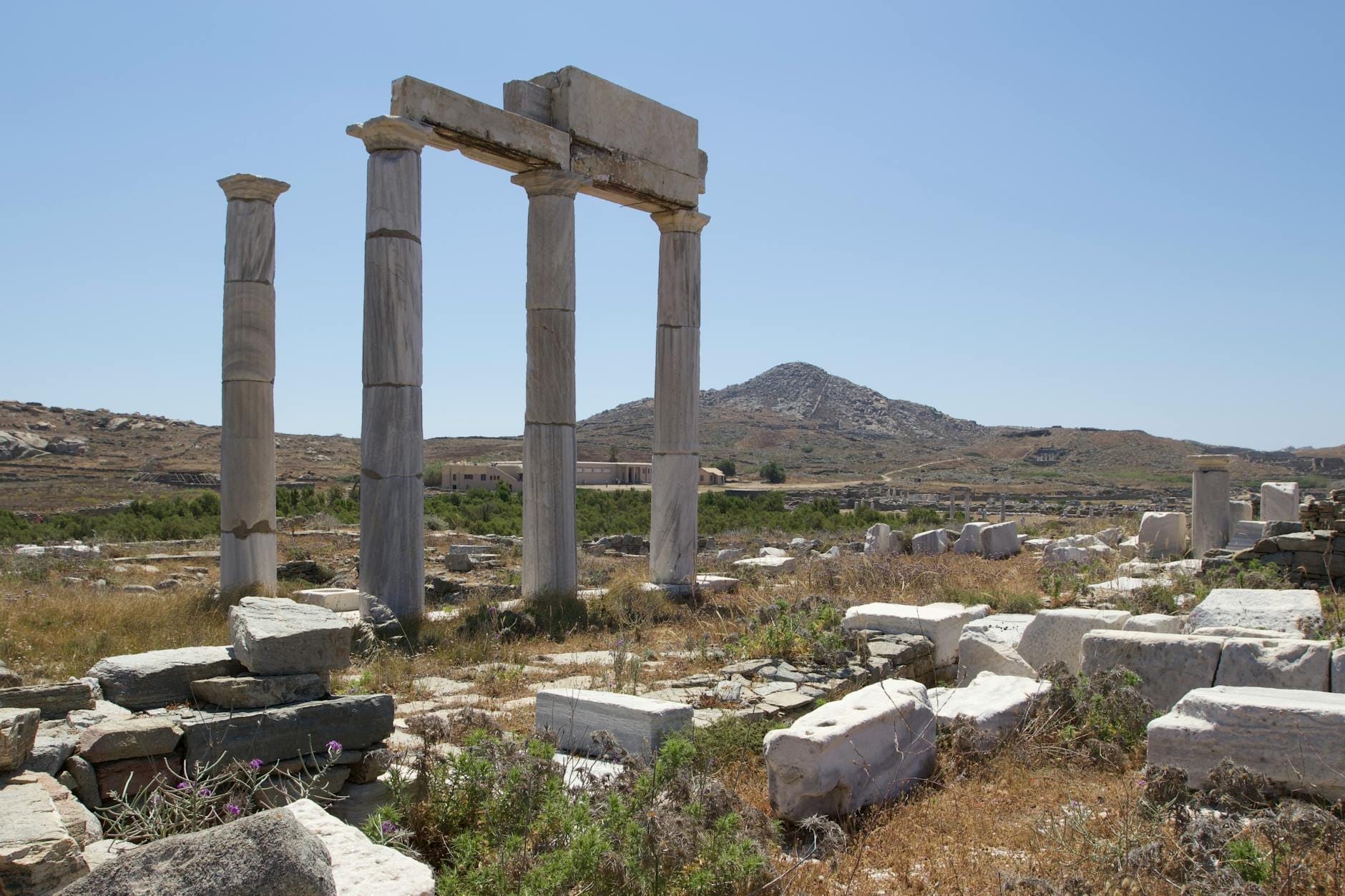 Antiguas columnas de mármol y ruinas en un yacimiento arqueológico abierto con una montaña al fondo bajo un cielo azul despejado.